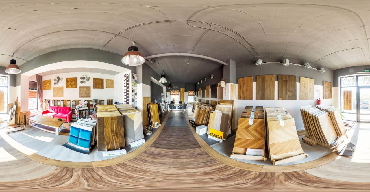 Wnętrze salonu z ekspozycją różnych wzorów i rodzajów okładzin podłogowych, w tym drewnianych i paneli, prezentowanych na stojakach i ścianach, z widocznym miejscem do konsultacji i wypoczynku...