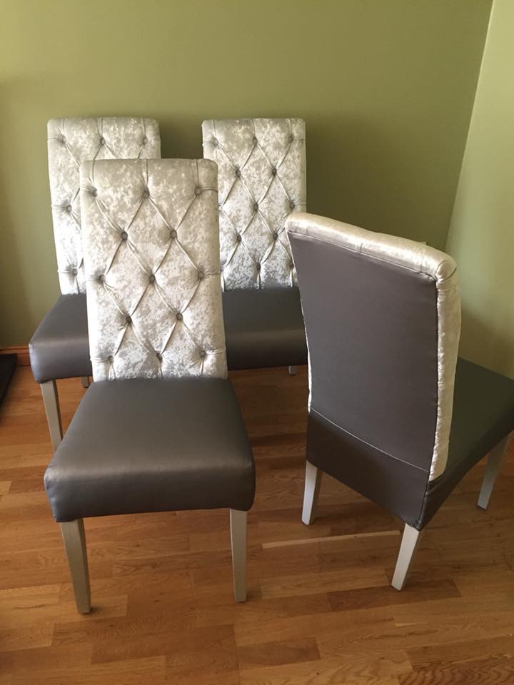 Cztery krzesła z szarymi siedziskami i srebrnymi, pikowanymi oparciami ustawione na drewnianej podłodze, jedno z nich odwrócone tyłem ukazujące gładki, szary materiał na plecach oparcia.