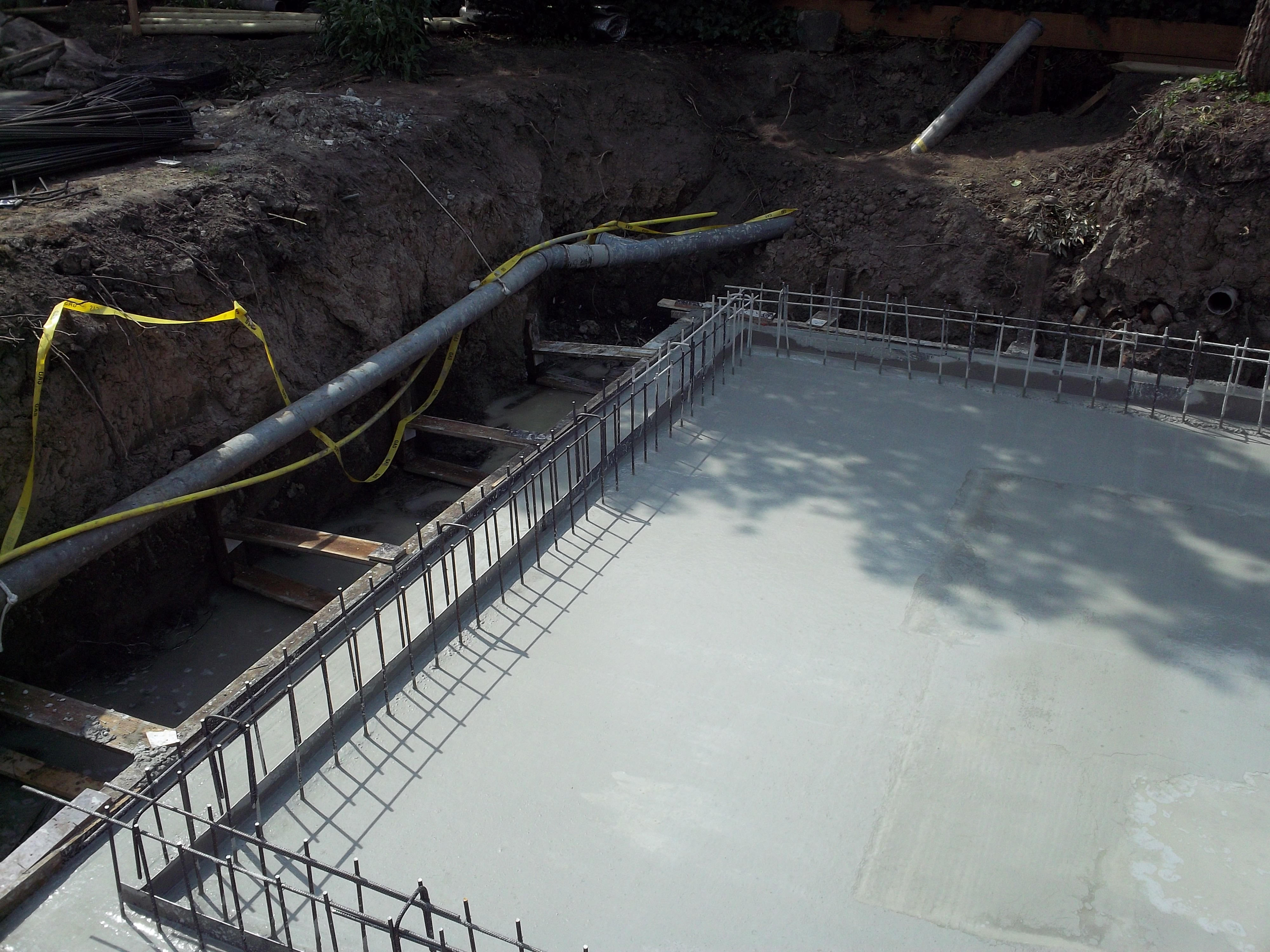 Wylany fundament zbrojony stalą na budowie w Jeleniej Górze, widoczne rury i taśma ostrzegawcza w wykopie.