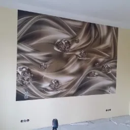 Ściana w pokoju po tapetowaniu z fototapetą w odcieniach brązu i beżu z motywem abstrakcyjnych fal i kryształowych kul, widoczne gniazdka elektryczne i narzędzia na podłodze.