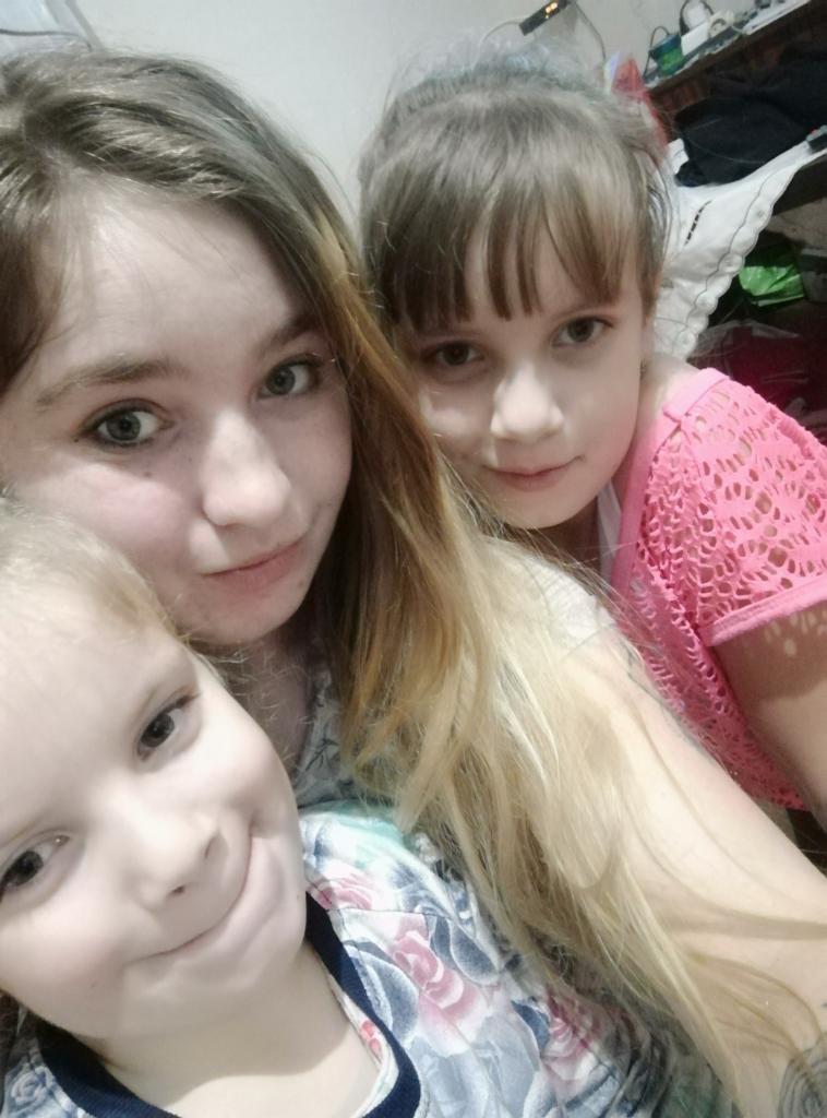 Portret selfie trzech dziewczynek o różnym wieku, uśmiechniętych, z widocznym fragmentem zagraconego pokoju w tle.