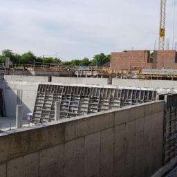 Izol-Mont Sp. z o.o. - Fundamenty domu w trakcie budowy, widoczne betonowe ściany szalunkowe, zbrojenia, konstrukcja murowana w tle oraz żuraw budowlany.