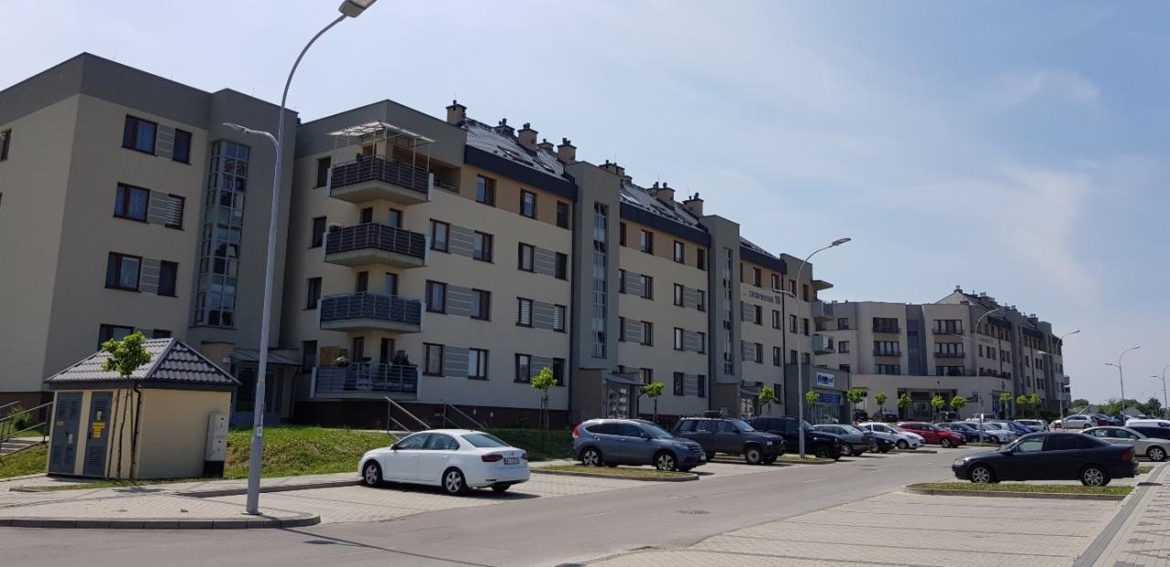 Nowoczesny budynek mieszkalny z balkonami w Rzeszowie, zlokalizowany przy parkingu z zaparkowanymi samochodami.