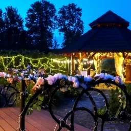 Oświetlona altana i dekorowany kwiatami mostek w ogrodzie, przygotowane na uroczystość wieczorową porą.