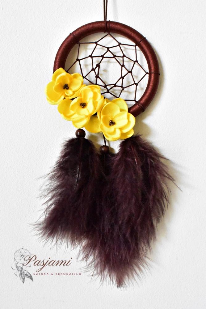 Ręcznie robiony łapacz snów z brązową obręczą, żółtymi kwiatami z filcu i bordowymi piórami, zawieszony na białym tle.