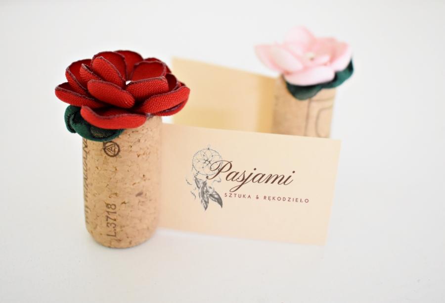 Ręcznie robione ozdoby: czerwona i różowa róża z materiału na korkach po winie, wizytówka 'Pasjami Sztuka i Rękodzieło' z motywem łapacza snów.