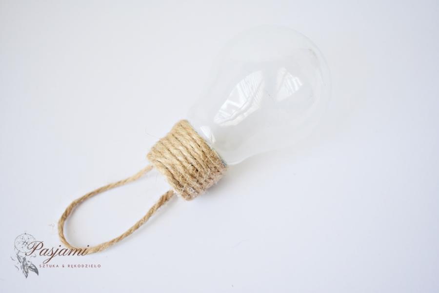 Szklana żarówka okręcona jutowym sznurkiem, tworząca dekoracyjny element z uchwytem, na białym tle.