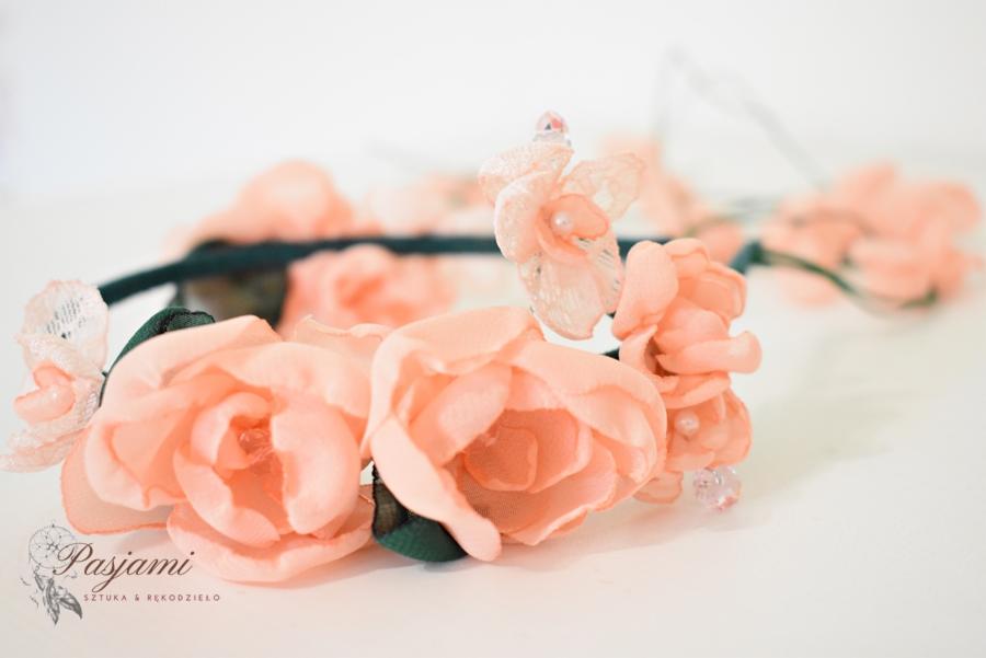 Delikatny wianek z brzoskwiniowych, materiałowych róż i perełek, wykonany ręcznie przez firmę z Mielca, widoczny na białym tle.