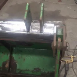 Fragment zielonej łyżki koparki po naprawie, widoczne nowe spawy i ślady zużycia farby.