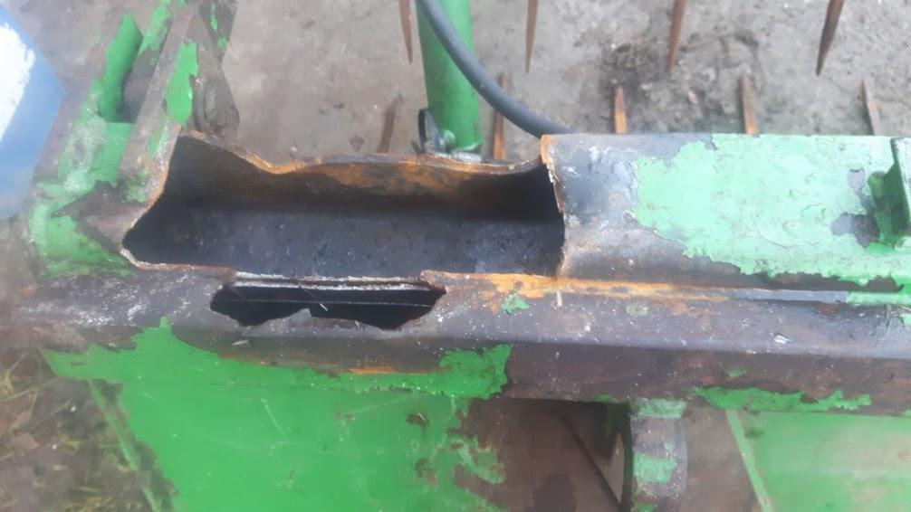 Fragment uszkodzonego, skorodowanego elementu metalowego maszyny rolniczej z odpryskującą zieloną farbą i widocznymi śladami rdzy.