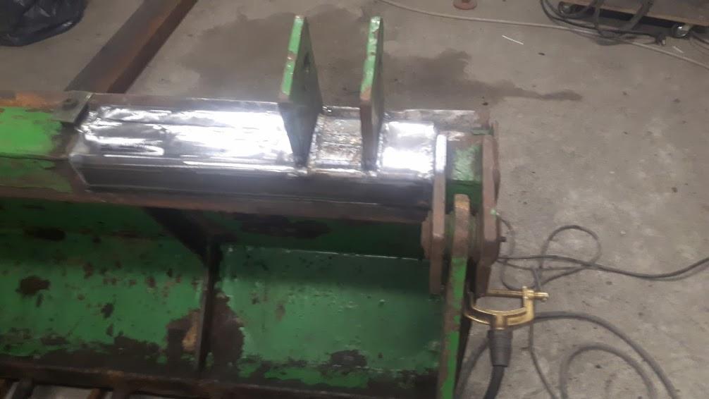 Fragment zielonej łyżki koparki po naprawie, widoczne nowe spawy i ślady zużycia farby.