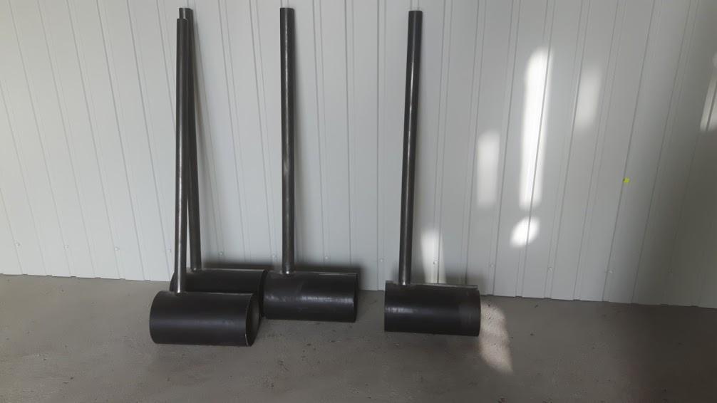 Metalowe konstrukcje spawane z rur i cylindrów, ustawione na szarej podłodze przy białej ścianie z panelami, widoczne ślady spawania.