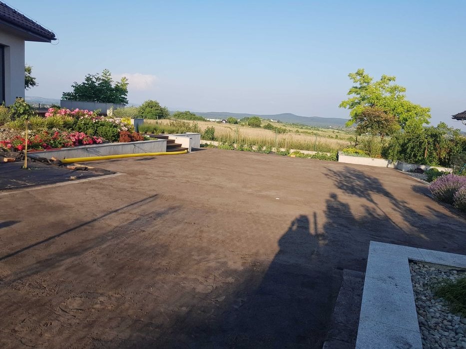 Przygotowany teren pod trawnik z widocznymi rabatami kwiatowymi i systemem nawadniania, w tle krajobraz wiejski.