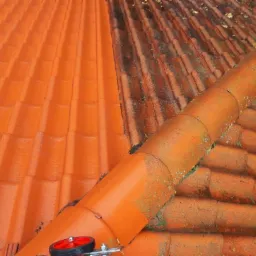 Częściowo umyty dach z pomarańczowej dachówki ceramicznej, widoczna różnica między czystą a brudną częścią, na dachu narzędzie z czerwonym kołem.