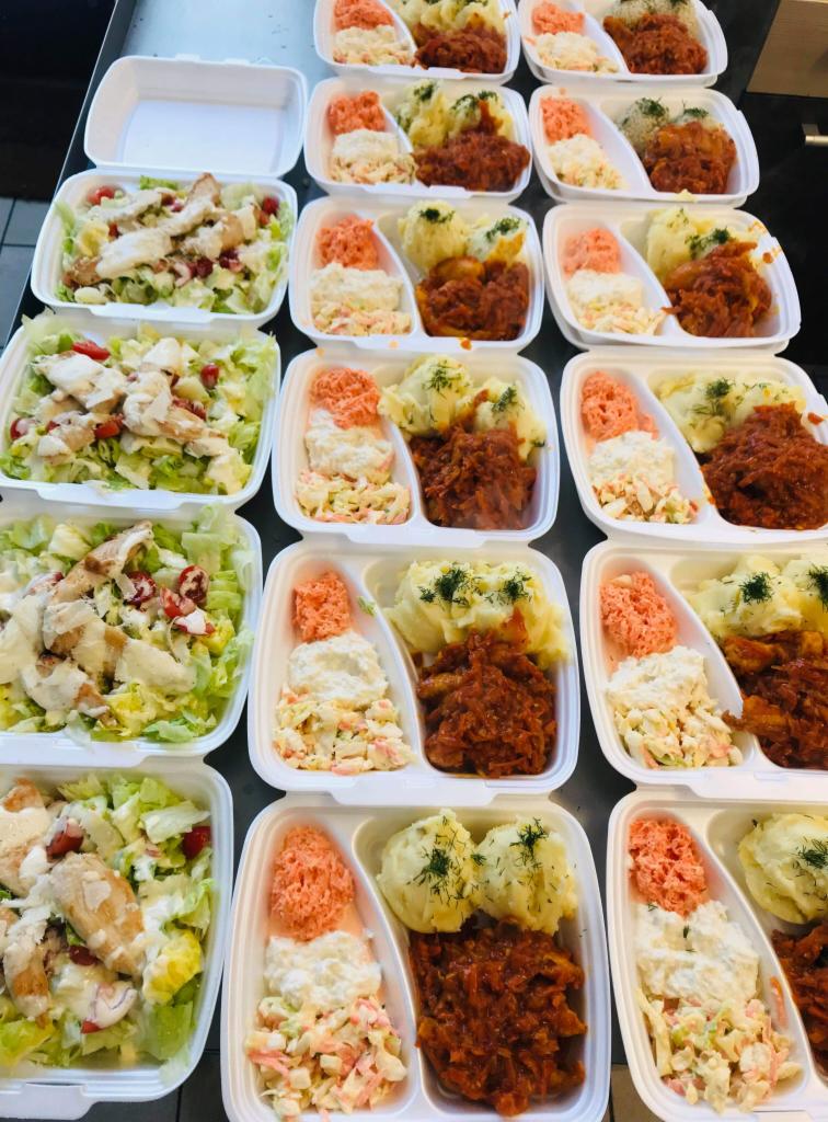 Rzędy plastikowych pojemników z gotowymi daniami: sałatka z kurczakiem, surówki i ziemniaki z koperkiem oraz gulasz warzywny.