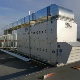 Zewnętrzna instalacja centrali wentylacyjnej VBW z kanałami na dachu budynku, widoczne elementy mocujące i zabezpieczenia.