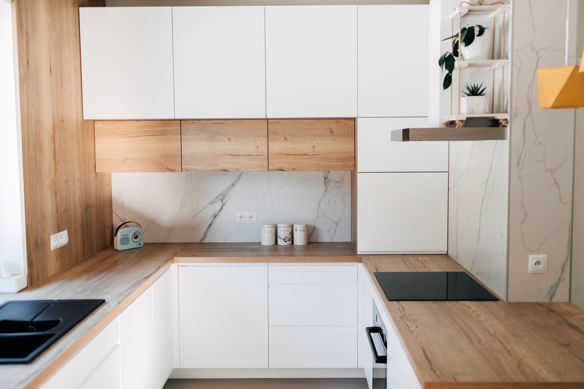 Jasna kuchnia w Tarnowie z białymi szafkami i drewnianymi blatami, uzupełniona o dekoracyjny radioodbiornik w stylu retro i marmurową ścianę.