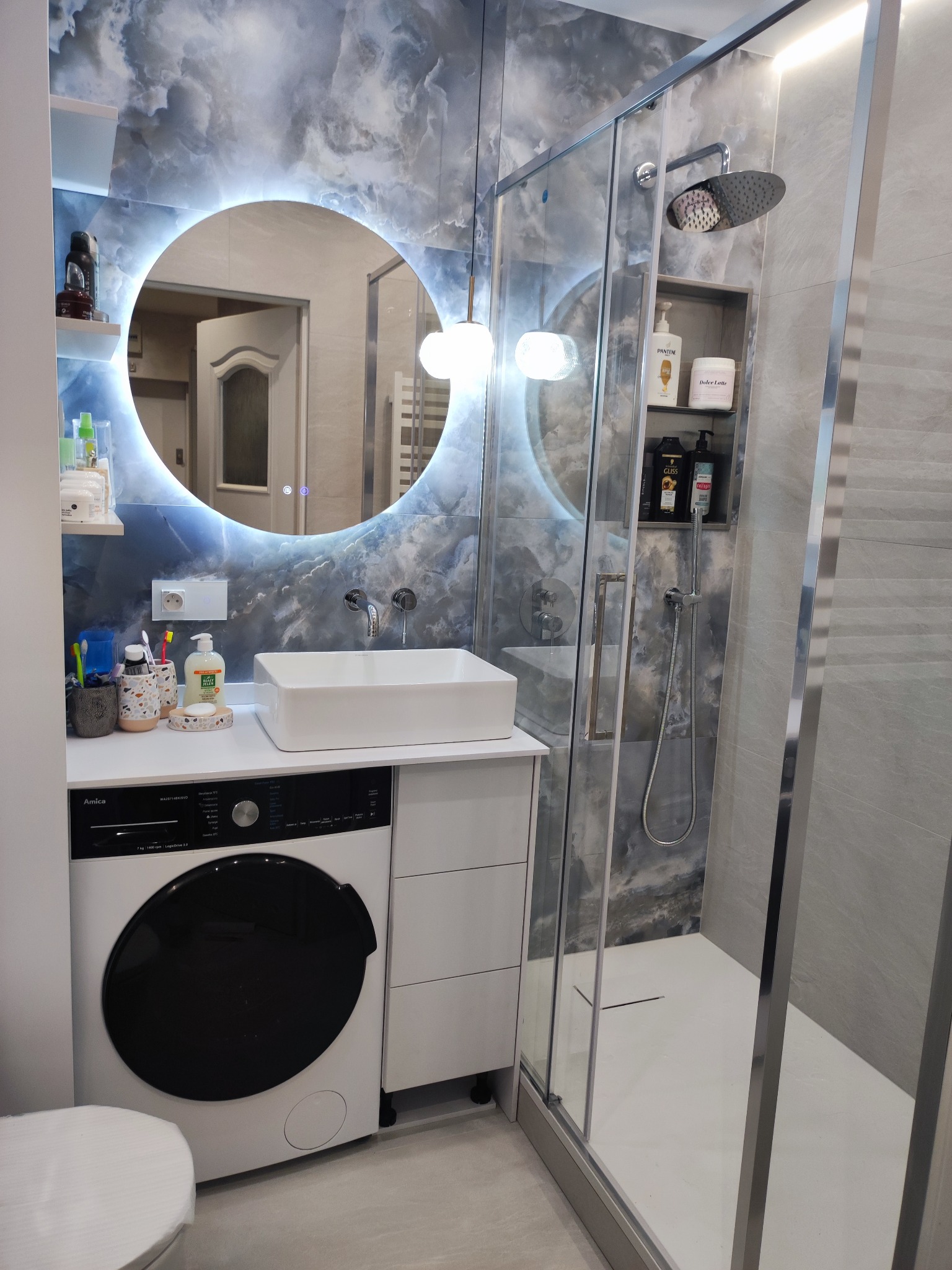 Nowoczesna łazienka z kabiną prysznicową, umywalką nablatową i okrągłym lustrem z podświetleniem LED. Na ścianach szare płytki imitujące marmur.