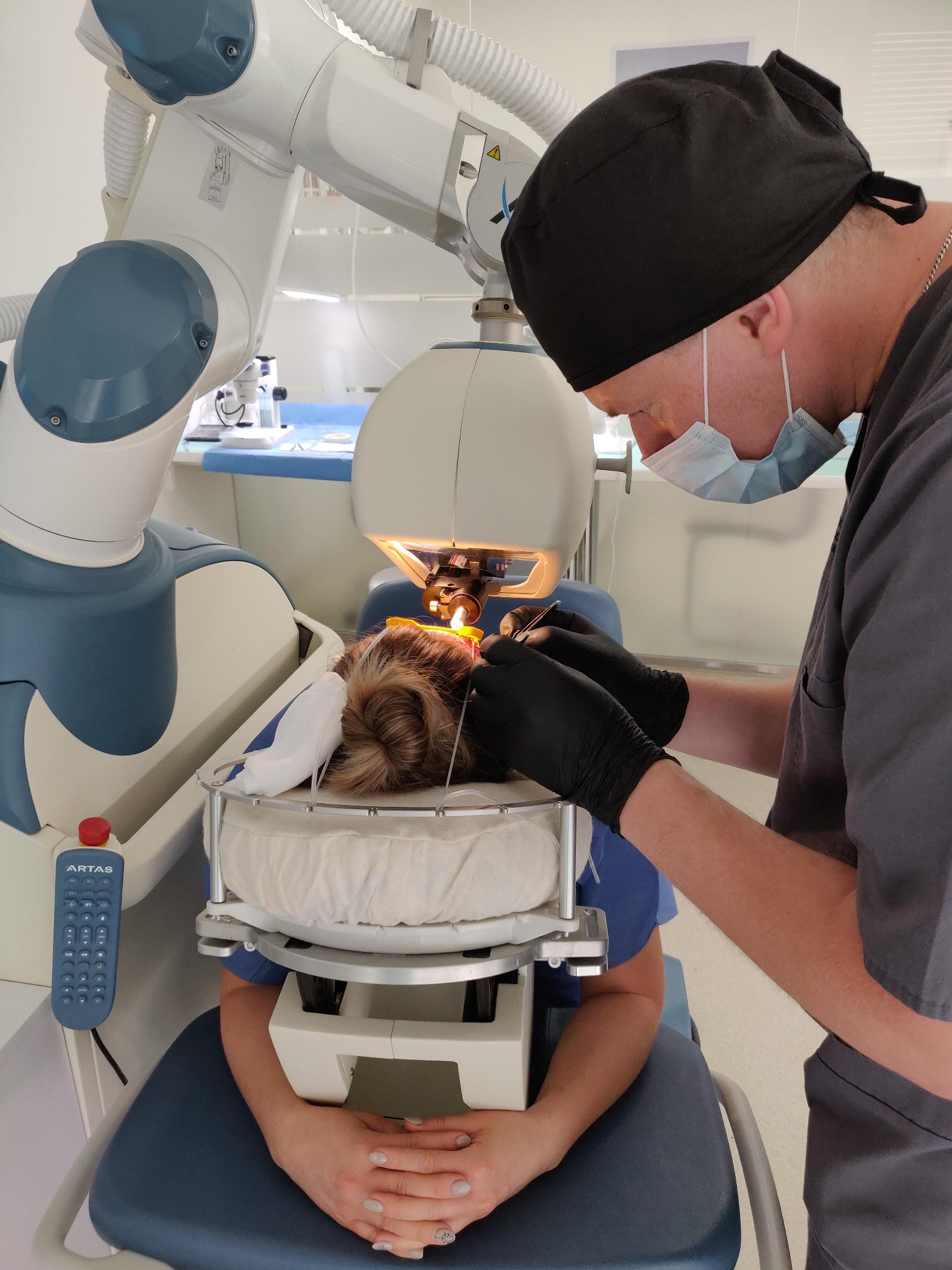 Pacjentka poddawana zabiegowi laserowej korekcji wzroku przy użyciu zaawansowanego robota medycznego, obsługiwanego przez lekarza w czepku i masce.