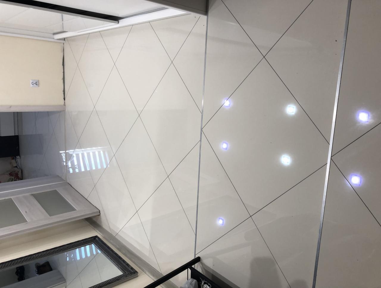 Połyskujące, kremowe płytki ułożone w romby z wbudowanymi punktowymi lampami LED w łazience z widocznym fragmentem lustra i drzwi.