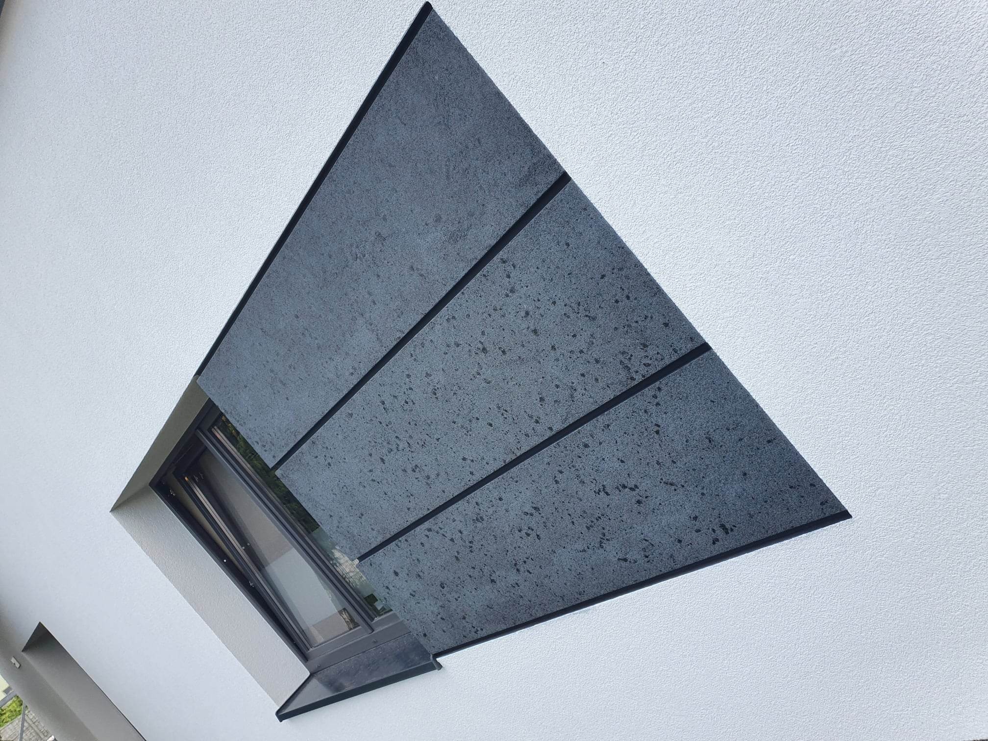 Biała elewacja z oknem i dekoracyjnym panelem w odcieniach szarości podzielonym na trzy segmenty czarnymi listwami, ujęcie z dołu.