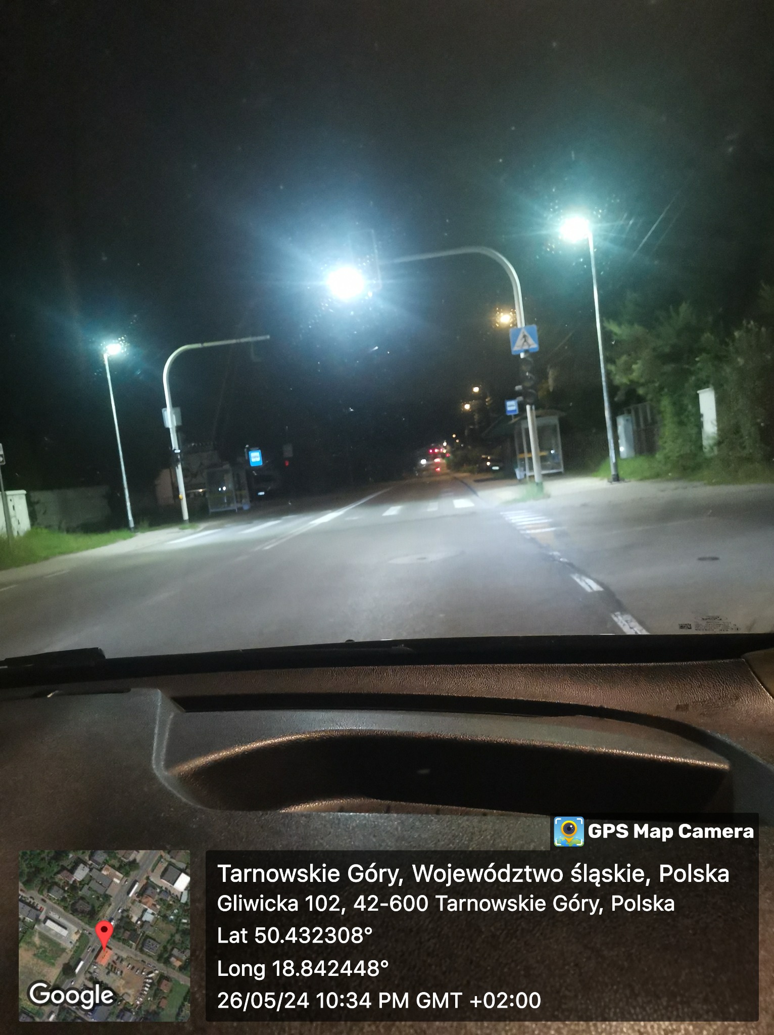 Nocny widok zza szyby samochodu na oświetloną ulicę w Tarnowskich Górach, z widocznym przystankiem i przejściem dla pieszych. Zdjęcie z lokalizacją i datą.