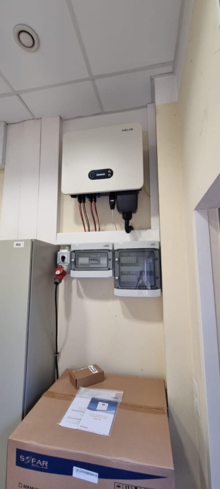 Zamontowany inwerter SOFAR z okablowaniem i rozdzielnicą na ścianie, obok szafka RG i karton z dokumentacją. Instalacja fotowoltaiczna w pomieszczeniu.