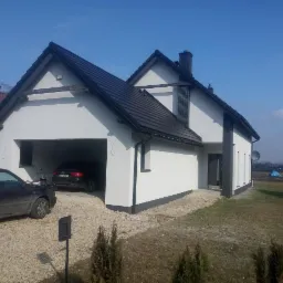 Nowoczesny dom jednorodzinny w Siemianowicach Śląskich z białą elewacją i ciemną dachówką, widok z zewnątrz na garaż z dwoma samochodami, błękitne niebo w tle.