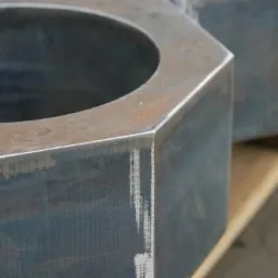 Detale dwóch stalowych, sześciokątnych nakrętek o dużych rozmiarach, z widocznymi śladami obróbki na krawędziach i powierzchni, umieszczonych na drewnianej palecie.