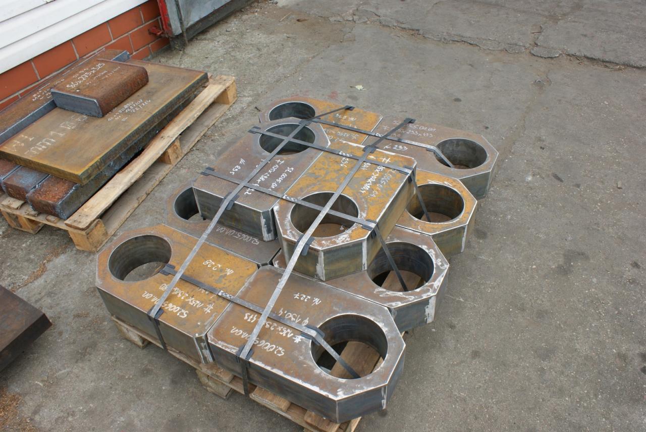 Elementy konstrukcyjne ze stali, z okrągłymi otworami, spięte taśmami na palecie w Tucznie, obok leżą płaskowniki.