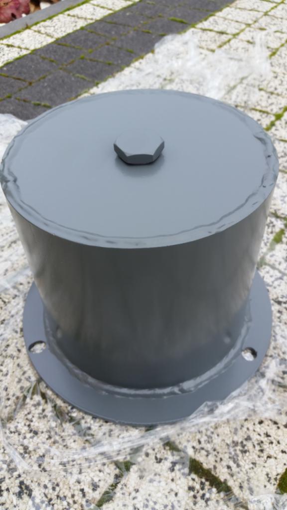 Szara, stalowa podpora kolumny z sześciokątną śrubą na wierzchu, umieszczona na zabezpieczonej folią powierzchni z kostki brukowej.