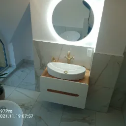 Nowoczesna łazienka na poddaszu z marmurowymi płytkami, owalną umywalką nablatową na drewnianym blacie i okrągłym lustrem z podświetleniem LED.