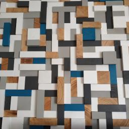 Usługi Remontowo-Budowlane Mateusz Pacuła - Dekoracyjna ściana z drewnianych i malowanych na biało, szaro i niebiesko klocków o różnych rozmiarach, tworząca trójwymiarową mozaikę.