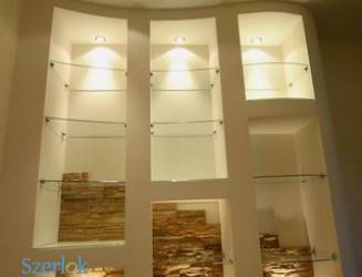 Wnęka w ścianie z półkami ze szkła i dekoracyjnym wykończeniem z kamienia naturalnego w dolnej części. Oświetlenie punktowe na górze każdej wnęki.