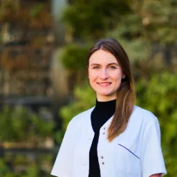 Uśmiechnięta dietetyczka w białym uniformie na tle zielonej ściany z roślin.