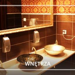 Hotel Korona-Palace *** - Elegancka łazienka z dwoma szklanymi umywalkami w odcieniach złota i brązu, ciemne płytki, ozdobne lustro w złotej ramie i wzorzysta tapeta.