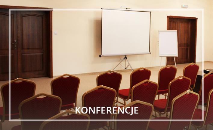 Sala konferencyjna z rzędami krzeseł z czerwonym obiciem, ekranem projekcyjnym i tablicą suchościeralną, przygotowana do prezentacji.