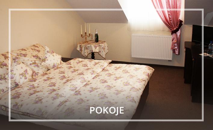 Pokój hotelowy na poddaszu z łóżkiem w kwiaty, stolikiem z szampanem i świecami, oraz zasłoniętym oknem.