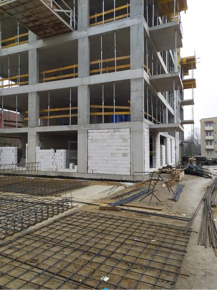 Wznoszony budynek z betonu i bloczków, widoczne zbrojenia fundamentów i szalunki na balkonach, stan surowy otwarty.