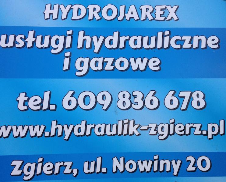 Niebieska tablica informacyjna z białym napisem 'HYDROJAREX usługi hydrauliczne i gazowe tel. 609 836 678 www.hydraulik-zgierz.pl Zgierz, ul. Nowiny 20', prezentująca zakres usług firmy.