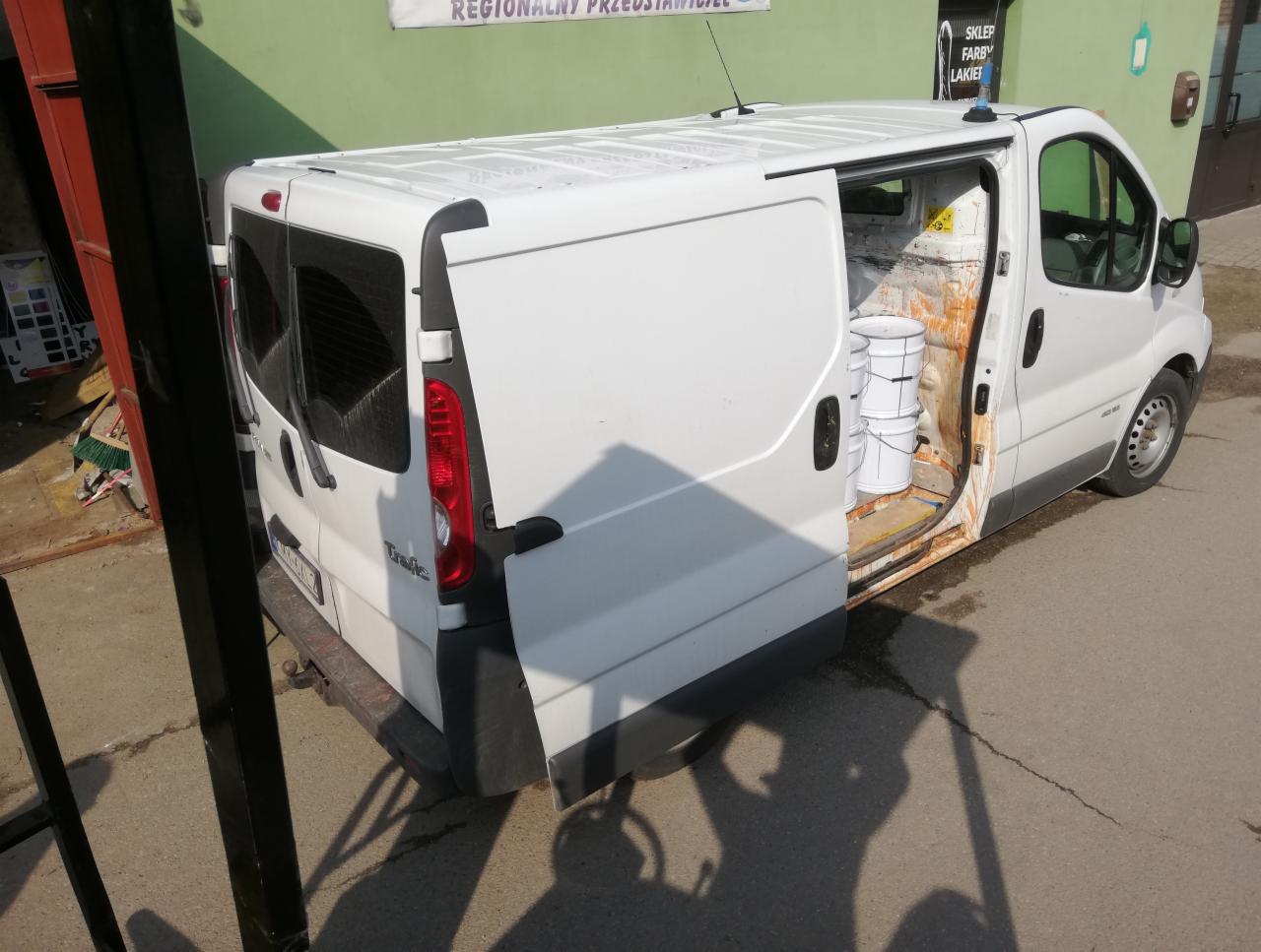 Biały bus Renault Traffic z otwartymi drzwiami bocznymi, wewnątrz widoczne trzy białe wiadra z farbą, ślady farby na progu i wewnątrz pojazdu.