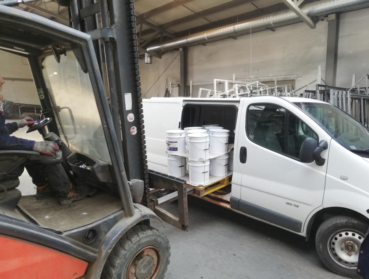 Wózek widłowy ładuje paletę z białymi wiadrami farby do białego busa w Sułkowicach, przygotowania do malowania.