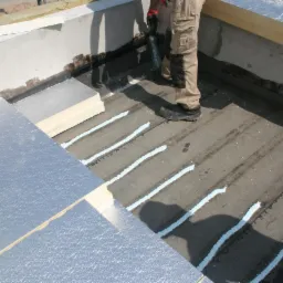 Prace izolacyjne: aplikacja kleju w pasmach na fundamencie pod płyty izolacyjne z folią aluminiową, widoczne fragmenty betonowego fundamentu.