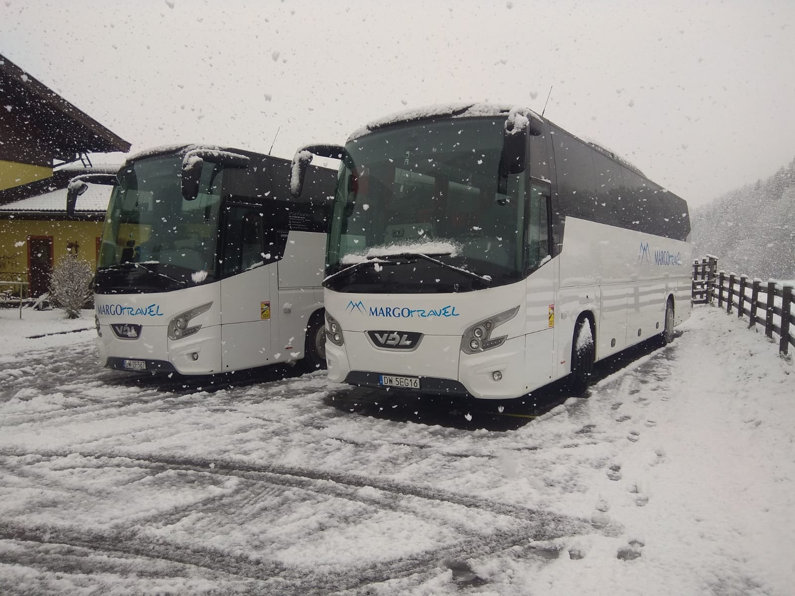 Dwa białe autokary firmy MargoTravel zaparkowane na śnieżnym parkingu w zimowy dzień, widoczne ślady opon na śniegu.