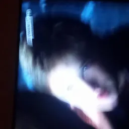 Rozmazane zdjęcie osoby z jasnymi włosami, zrobione prawdopodobnie z ekranu telewizora, z widocznymi artefaktami i słabym oświetleniem.