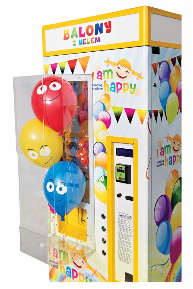 Automat vendingowy z balonami na hel z nadrukowanymi uśmiechniętymi twarzami, dekorowany rysunkami i napisem 'I am happy vending machine'.