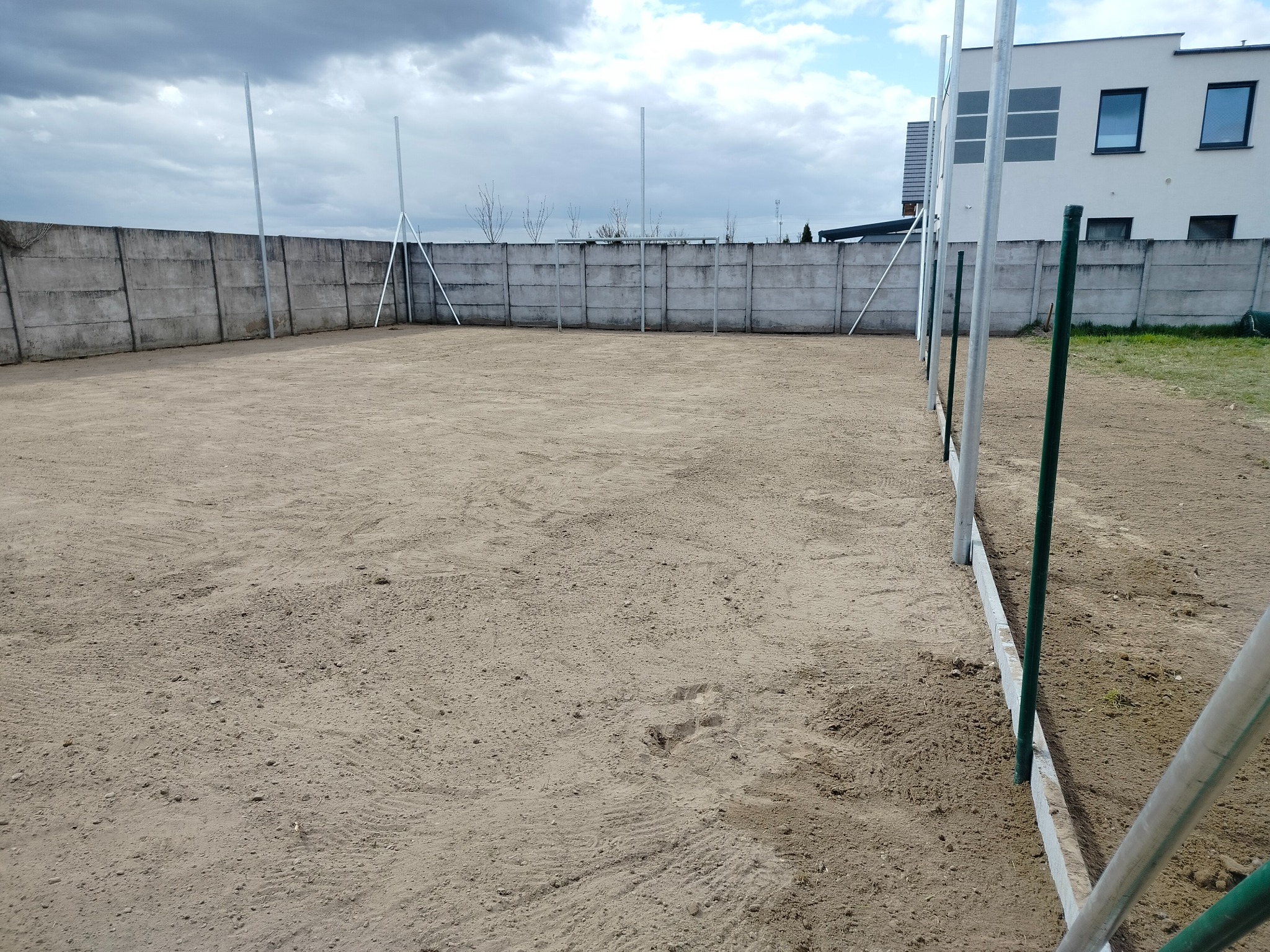 Przygotowany teren pod budowę ogrodzenia panelowego w Suchym Lesie. Widoczny wyrównany grunt, słupki montażowe i betonowy mur w tle.