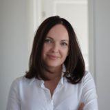 Portret kobiety z ciemnymi włosami, ubranej w białą koszulę, z delikatnym uśmiechem, na jasnym tle.