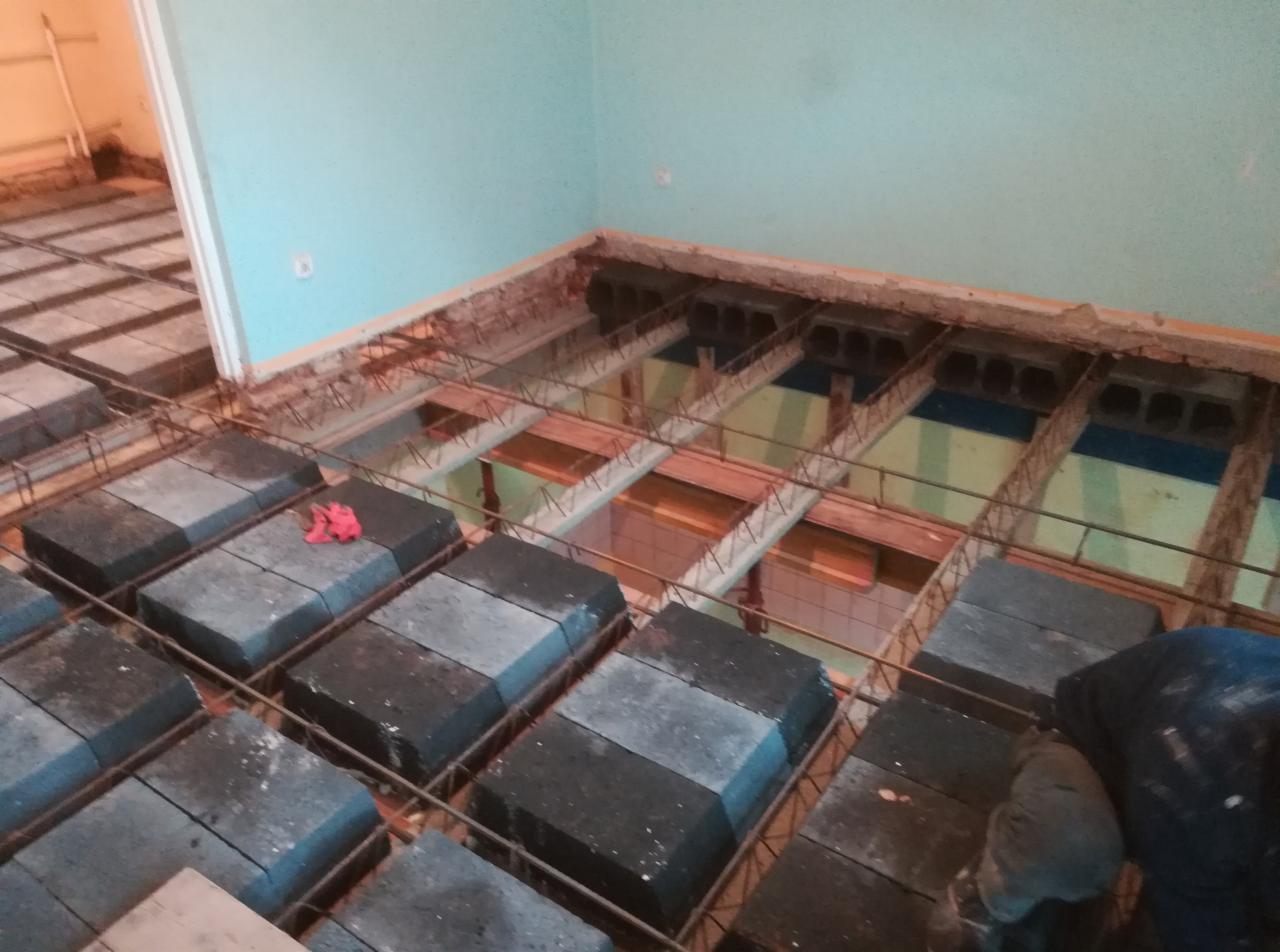 Przygotowanie szalunku traconego z betonowych bloczków i zbrojenia stalowego pod wylewkę fundamentu wewnątrz budynku z błękitnymi ścianami.