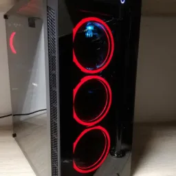 Czarna obudowa komputera stacjonarnego z przeszklonym bokiem, podświetlana trzema czerwonymi wentylatorami i dwoma niebieskimi diodami na górze, stojąca na drewnianym blacie.